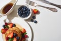 Top view of delicious pancakes with blueberries and strawberries on plate near cutlery and maple syrup in gravy boat on marble Royalty Free Stock Photo