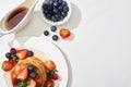 Top view of delicious pancakes with blueberries and strawberries on plate near maple syrup in gravy boat on marble white surface Royalty Free Stock Photo