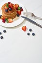 Top view of delicious pancakes with maple syrup, blueberries and strawberries on plate near fork and knife on marble white surface Royalty Free Stock Photo