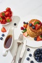 Top view of delicious pancakes with maple syrup, blueberries and strawberries on plate near fork and knife on marble white surface Royalty Free Stock Photo