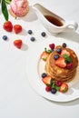 Top view of delicious pancakes with maple syrup, blueberries and strawberries on plate near rose flower on marble white surface Royalty Free Stock Photo