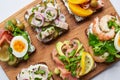 Top view of delicious smorrebrod sandwiches on wooden chopping board on white.