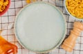 top view of different macaronis in bowls salt butter around plate on plaid cloth background