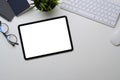 Top view of tablet with empty screen, glasses, plant and keyboard on white office desk.