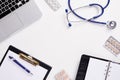 Top view of doctor desk with stethoscope, latptop, pills and blank paper on clipboard with copy space