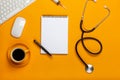 Top view of a doctor`s table with notepad and pen stethoscope, keyboard, prescription and pills, a cup of coffee on a yellow Royalty Free Stock Photo