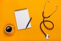 Top view of a doctor`s table with notepad and pen stethoscope, keyboard, prescription and pills, a cup of coffee on a yellow