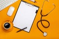 Top view of a doctor`s table with notepad and pen stethoscope, keyboard, prescription and pills, a cup of coffee on a yellow Royalty Free Stock Photo