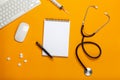 Top view of a doctor`s table with notepad and pen stethoscope, keyboard, prescription and pills, a cup of coffee on a yellow Royalty Free Stock Photo