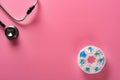 Top view daily doses pills in plastic container and a stethoscope on pink background Royalty Free Stock Photo