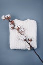 Top view of dried branch of cotton flowers on cozy white sweater on grey background. Flat lay.