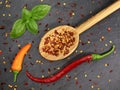 Top view of dried chili flakes and seeds in wooden cooking spoon with red and orange chillies on black slate board Royalty Free Stock Photo