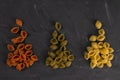 Top view of dry conchiglie pasta on black board background. Three triangular slides with pasta conchiglie spread out in colors,