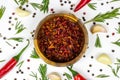 Top view of dry red chili pepper slices in a round wooden bowl with peppercorns, garlic and rosemary on white food background. Royalty Free Stock Photo