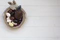 Top View Of Easter Bunny Basket With Chocolate Almond Eggs On White Wooden Table With Copy Space