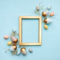 Top view of Easter eggs colored with in different colors arranged around a golden photo frame. Blue background. Copy space Royalty Free Stock Photo