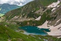 A top view of an emerald mountain lake with a snow cap surrounded by green mountain slopes