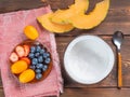 Top view of empty coconut bowl and blueberries and strawberries and melon and kumquat and teaspoon on a wooden background