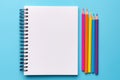 Top view of empty notebook with colorful crayon pencils on pastel blue background