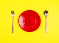 Top view of empty red dish with spoon and fork on vibrant yello Royalty Free Stock Photo