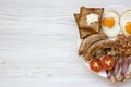 Top view English breakfast with fried eggs, bacon, sausages, beans and toasts. White wooden background.