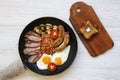 Top view, English breakfast in a pan with fried eggs, bacon, beans, sausages and toasts on a white wooden