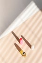 Top view of erfume roller bottle and hygienic lipstick in striped shadow background.