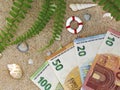 Top view of euro banknotes in the sand with shells and lifebuoy, concept of saving money for vacation Royalty Free Stock Photo