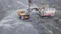 Top view of excavator in open pit. Excavator falls asleep rubble in dumper on outdoor quarry in extraction of minerals