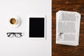 top view of eyeglasses, coffee cup, and digital tablet with blank screen on white and pile of newspapers on wooden background