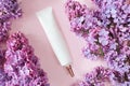 Top view of face and eye cream squeeze, cosmetic tube with long nozzle and bronze screw cap and pink lilac flowers on a powdery