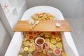 Faceless female in bathtub with slices of oranges, lemon and grapefruits is reading the book. Woman having detox bath