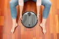 Top view of Faceless middle section of young woman seated at floor holding an intelligent vacuum cleaner to clean the floor