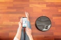 Top view of faceless middle section of young woman using smart phone to control an automatic vacuum cleaner to clean the floor, ma