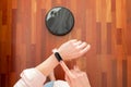 Top view of faceless middle section of young woman using smart watch to control an automatic vacuum cleaner to clean the floor, ma