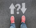 Top view of feet and different direction arrows with question mark on asphalt road