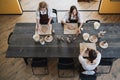 Top view of female artists sculpting different clay products on a big wooden table with pottery tools on it during a