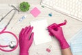 Top view of female doctor hands in gloves write in a notebook. Medical workplace with stethoscope, keyboard, thermometer and
