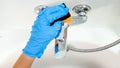 Top view of female hand in blue rubber glove washing and polishing water tap. Housewife cleaning faucet with sponge and Royalty Free Stock Photo