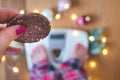 Top view of a female hand holding a cookie and scales with Christmas decorations and lights on wooden background Royalty Free Stock Photo