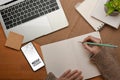 Female hand writing on blank notebook on worktable with laptop and smartphone Royalty Free Stock Photo