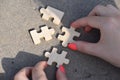 Top view of female hands connecting wooden puzzle pieces, shadow on the ground