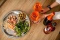 Top view of female hands hold two glasses of cold bright orange drink which stands on the table