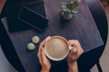 Top view female hands holding hot cup of coffee above workspace with notebook, smartphone, sweets and green potted plant on dark Royalty Free Stock Photo