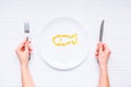 Top view female hands holding knife and fork under round plate with Cod Liver Oil Capsules, Omega 3, Vitamin D in the fish shape o Royalty Free Stock Photo