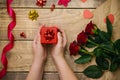 Top view, female hands holding a red gift box. Festive atmosphere, red roses and bows on a wooden background Royalty Free Stock Photo