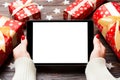 Top view of female hands holding a tablet on wooden Christmas background made of gift boxes and snowflakes. New year Royalty Free Stock Photo