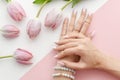 Top view female hands with a manicure and drawing on nails. Arrangement with pink tulip flowers and pearls on white and