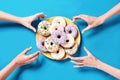 Top view of female hands taking colourful round glazed donuts with sprinkles from the plate over blue background, top