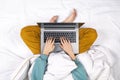 Top view on female hands working on modern laptop from bed at home. Home office or online education concept. Laptop lies on a Royalty Free Stock Photo